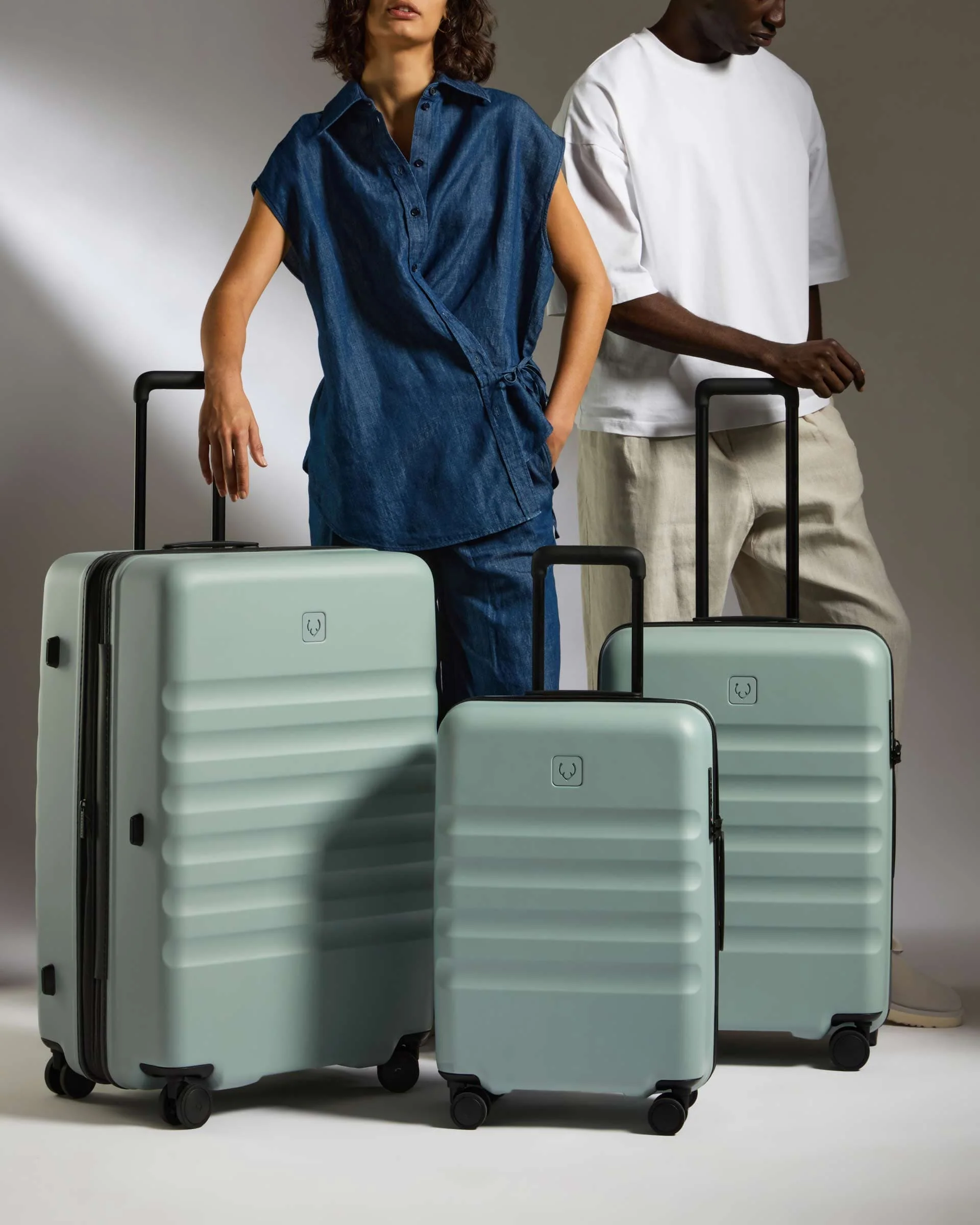 Two models standing with Antler suitcases in a studio scene.