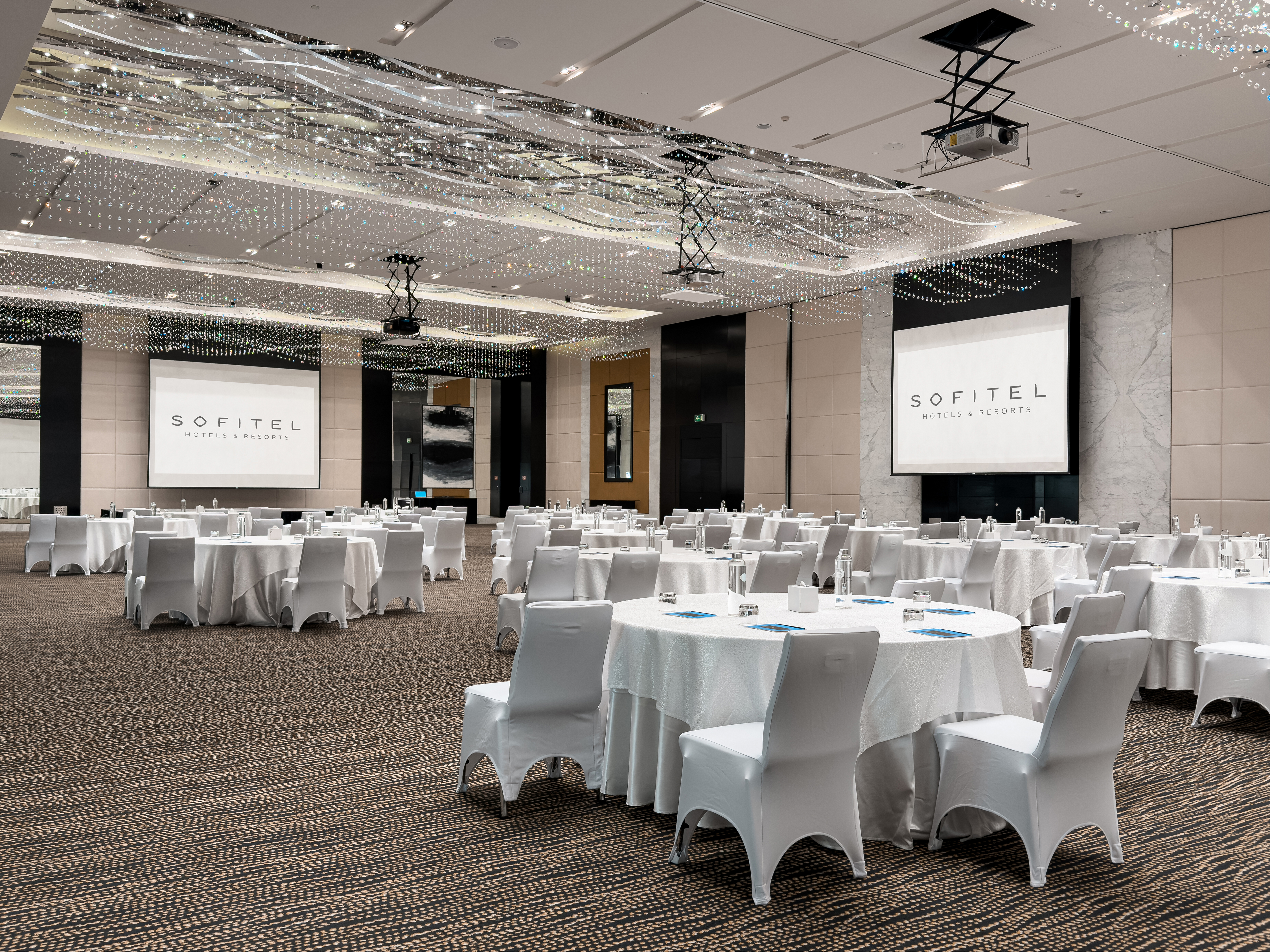 Ballroom at Sofitel Abu Dhabi Corniche with round event tables and branded screens.